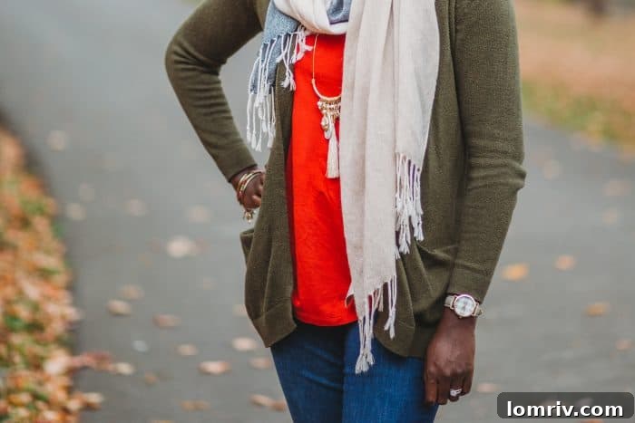 Full body shot of a woman in a cozy green fall sweater, accessorized with a patterned scarf, blue jeans, and brown leather boots, perfect for a casual autumn day.