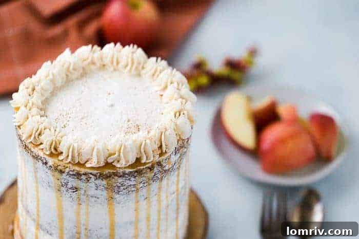Close-up of a slice of apple spice layer cake revealing moist crumb and apple pieces, topped with rich cinnamon frosting.