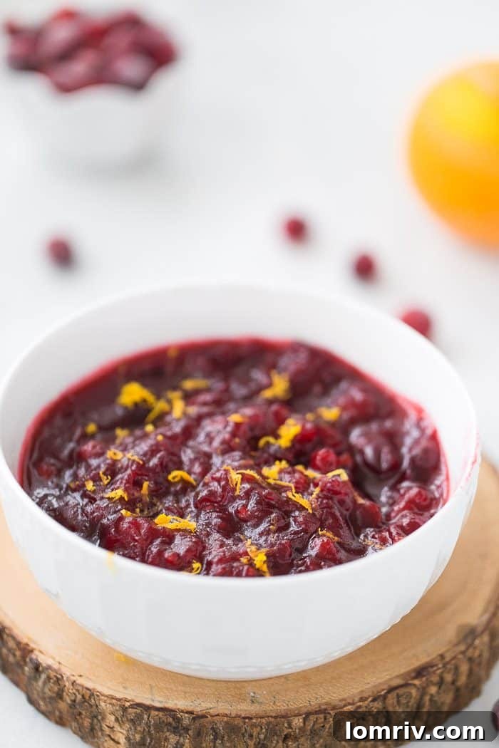 A bowl of homemade cranberry sauce adorned with orange slices and fresh cranberries