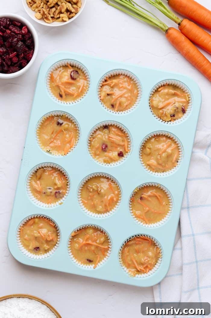 A blue cupcake tray filled with uncooked cupcake batter, carrots blurred in the background.