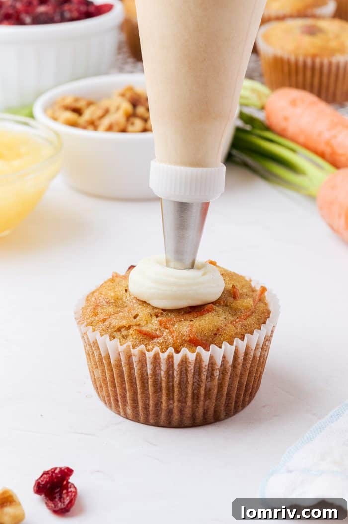 A carrot cake cupcake being expertly topped with luscious frosting.