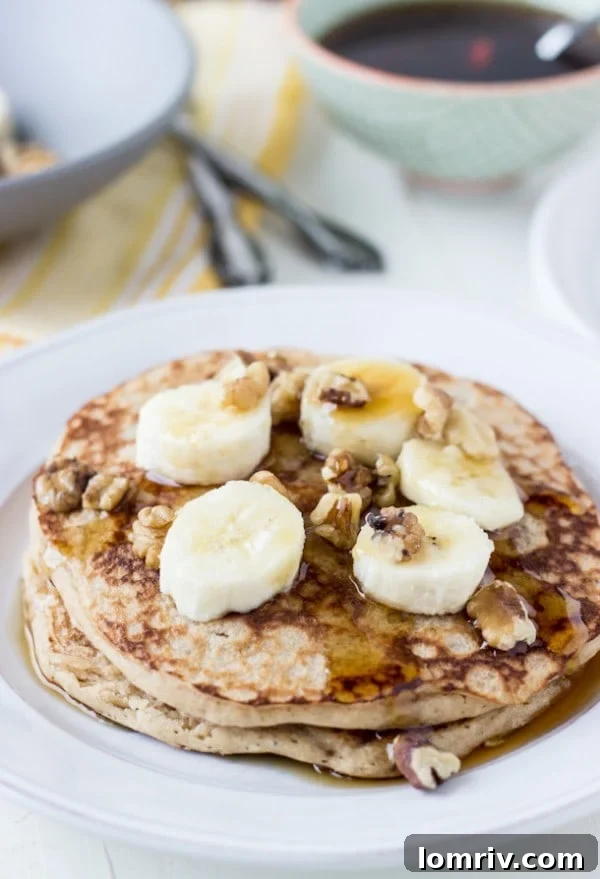 Fluffy Whole Wheat Banana Walnut Pancakes stacked high with syrup and fresh fruit, a perfect vegan breakfast or brunch option.