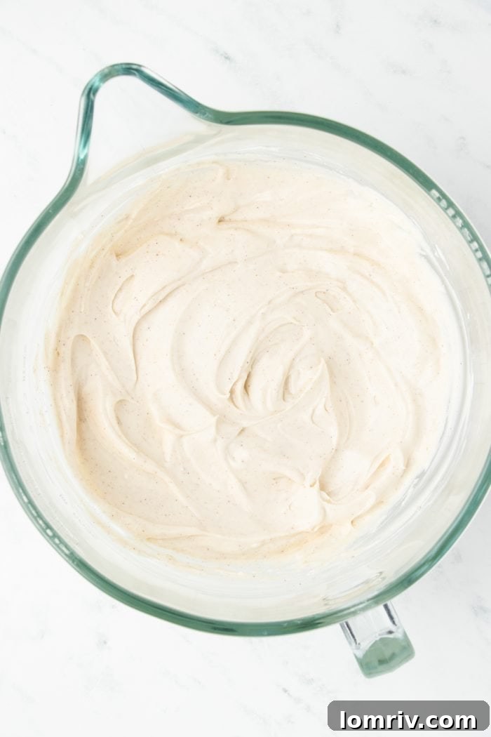 A mixing bowl with cream cheese, sugar, and pumpkin spice added to it.