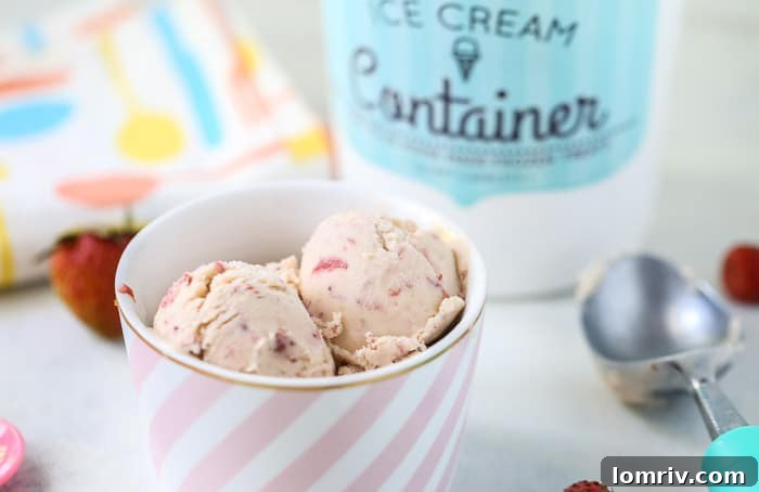 Scoops of homemade strawberry ice cream in a white bowl, garnished with a single fresh strawberry.