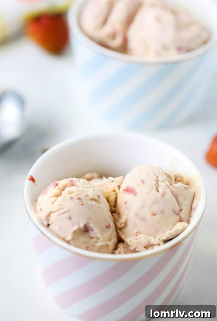 A generous scoop of homemade strawberry ice cream on a cone, with fresh strawberries in the background.