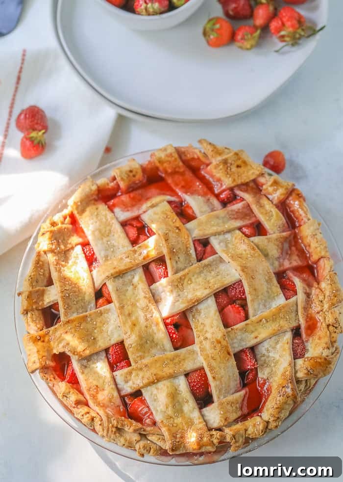 A picture of a homemade strawberry pie on a table with a bowl of fresh strawberries. The pie has a beautiful golden-brown lattice crust.