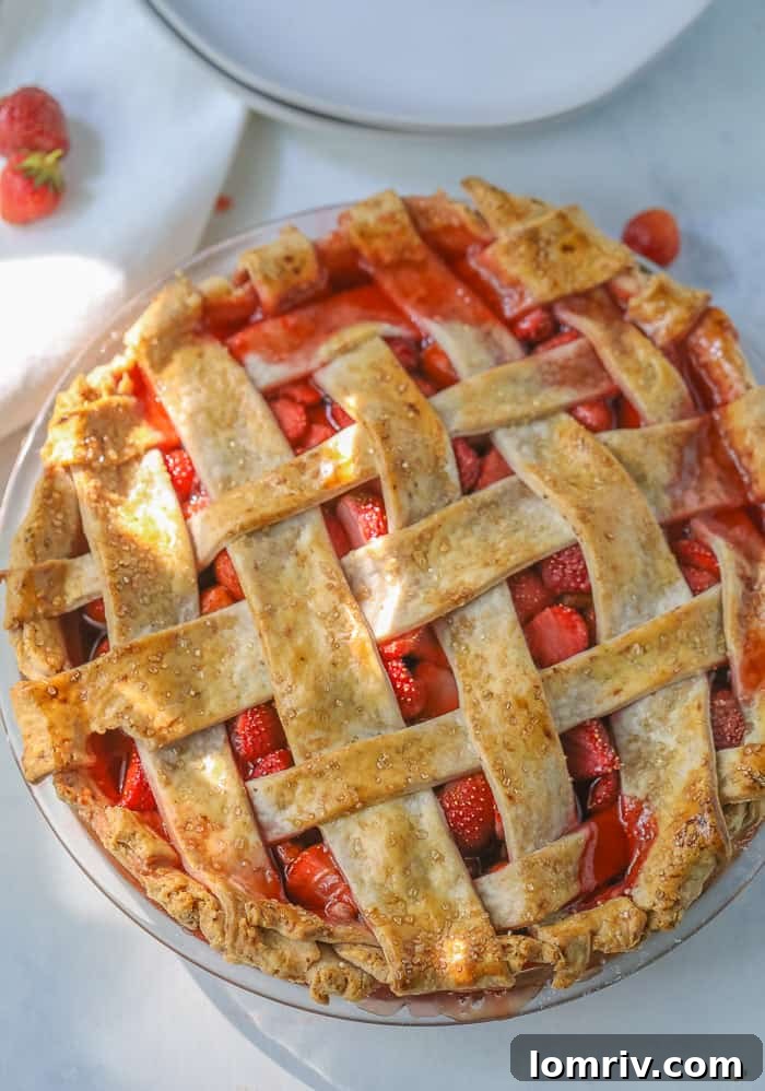 A close-up of a freshly baked homemade strawberry pie, with golden crust and hints of bubbly, sweet strawberry filling, garnished with fresh berries.