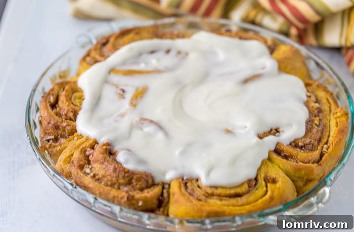 Maple Cream Cheese Icing being drizzled over freshly baked Pumpkin Cinnamon Rolls