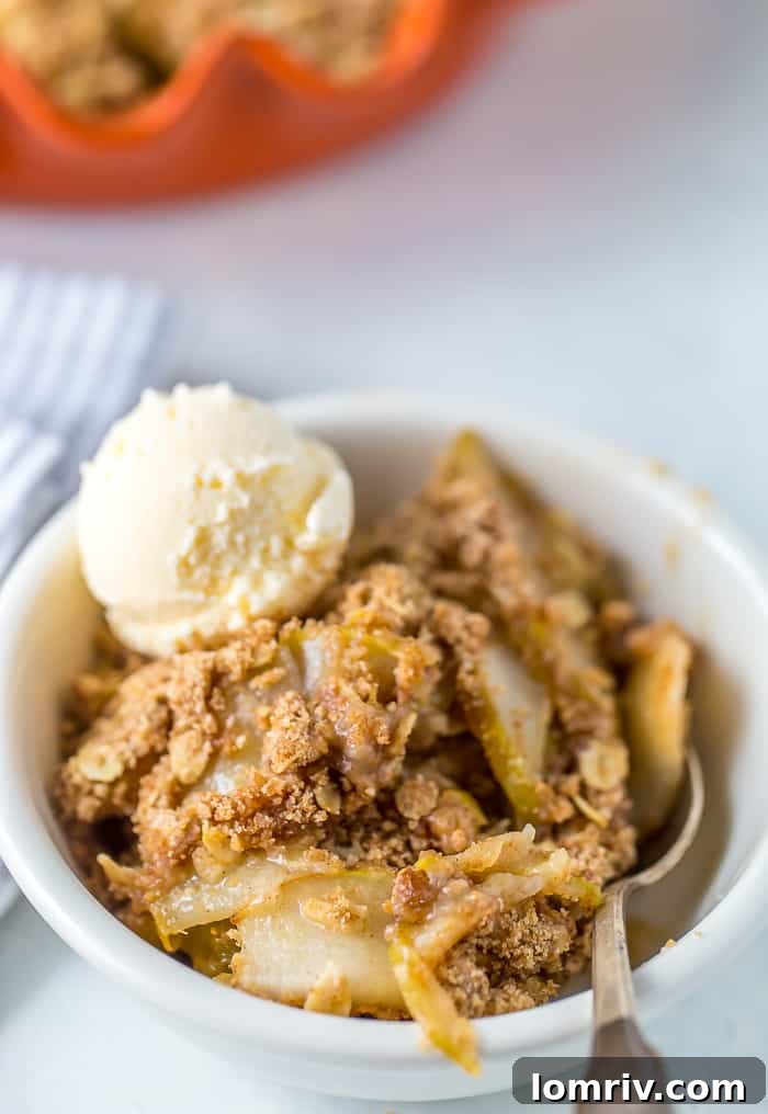 Delicious pear crisp, topped with a golden oat crumb and served with a scoop of melting vanilla ice cream in a white bowl.