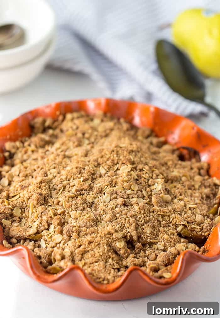 Close-up shot of a baked pear crisp with a crispy oat topping, showing the golden brown texture and bubbling fruit underneath.