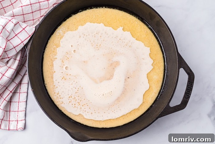 A Gingerbread Dutch Baby Pancake baking in a cast-iron skillet, showing its dramatic puff