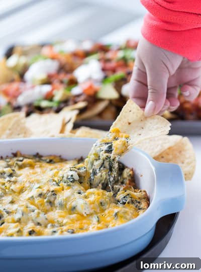 Crispy tortilla chip generously scooped with cheesy spinach artichoke dip, showing melted cheese