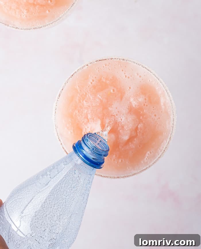 Two hands holding a freshly garnished Frozen Grapefruit Margarita with a sugar and salt rim.