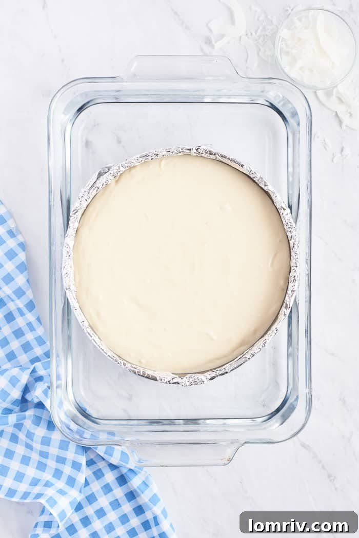 An unbaked Coconut Cheesecake, with its smooth filling settled in the crust, ready for the water bath.