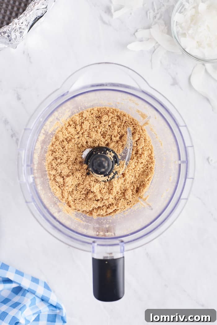 Graham cracker, coconut flakes, and coconut oil blended together to form a moist, sandy crust mixture for the cheesecake.