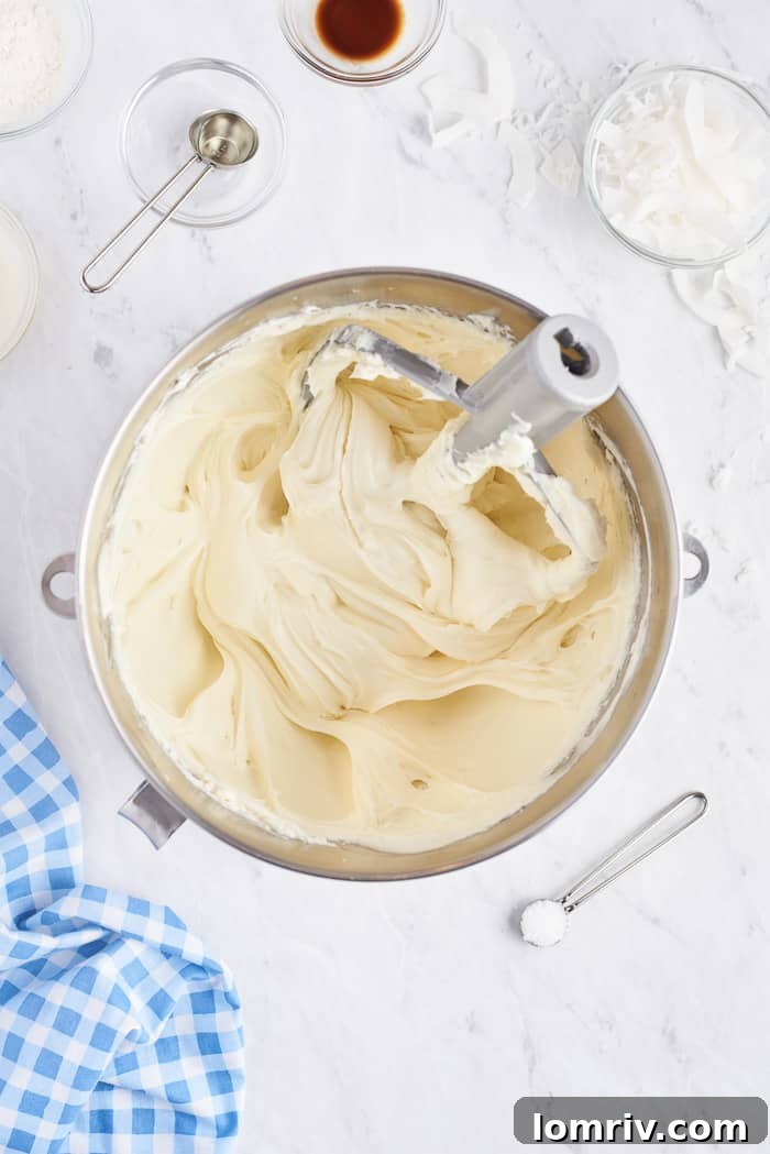Softened cream cheese being beaten to a smooth, creamy consistency in an electric mixer bowl.