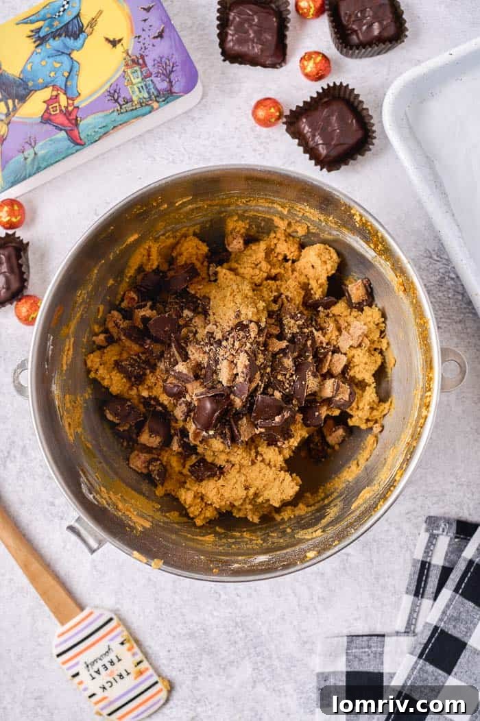 Chopped See's Dark Chocolate Peanut Crunch being gently folded into the pumpkin cookie dough with a spatula.