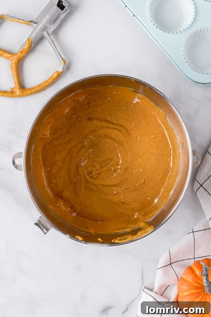 Wet ingredients for pumpkin cupcakes, including pumpkin puree and vanilla, being mixed