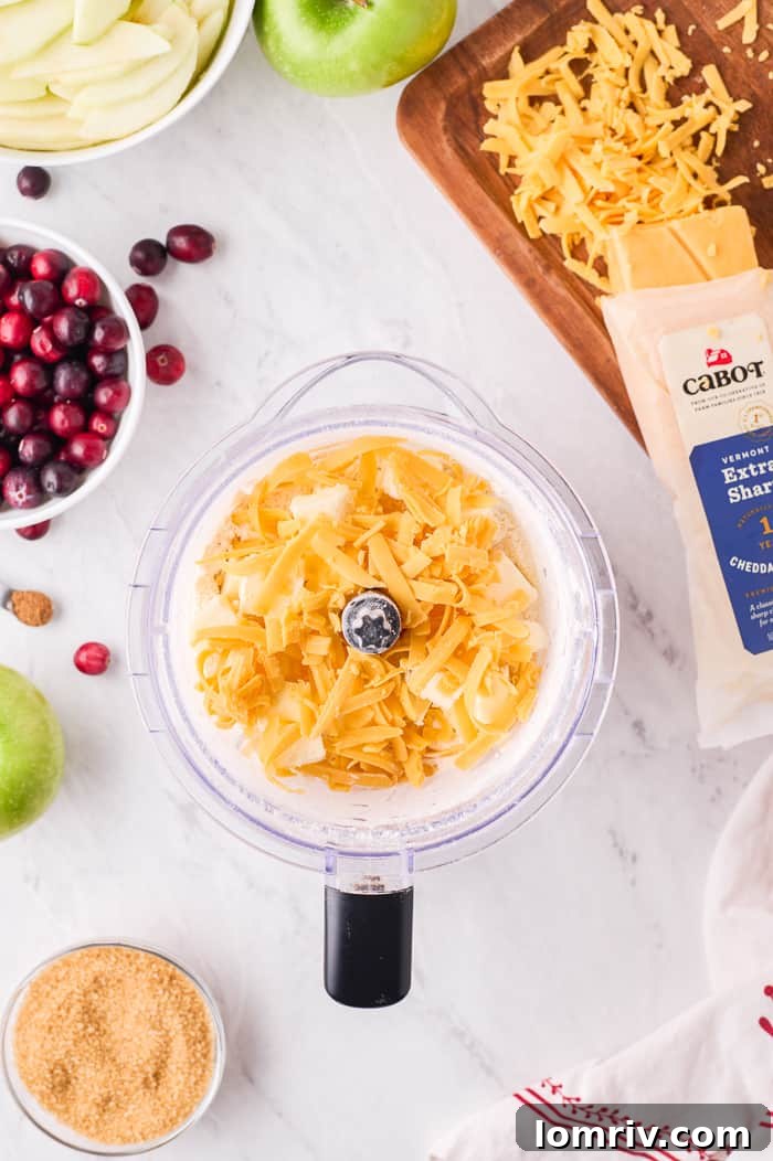 Food processor containing flour, butter, and grated cheddar cheese, mid-process for pie dough