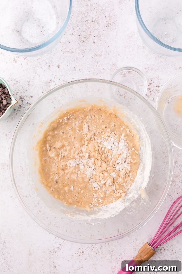 Adding dry ingredients to the wet mixture for banana chocolate chip muffins