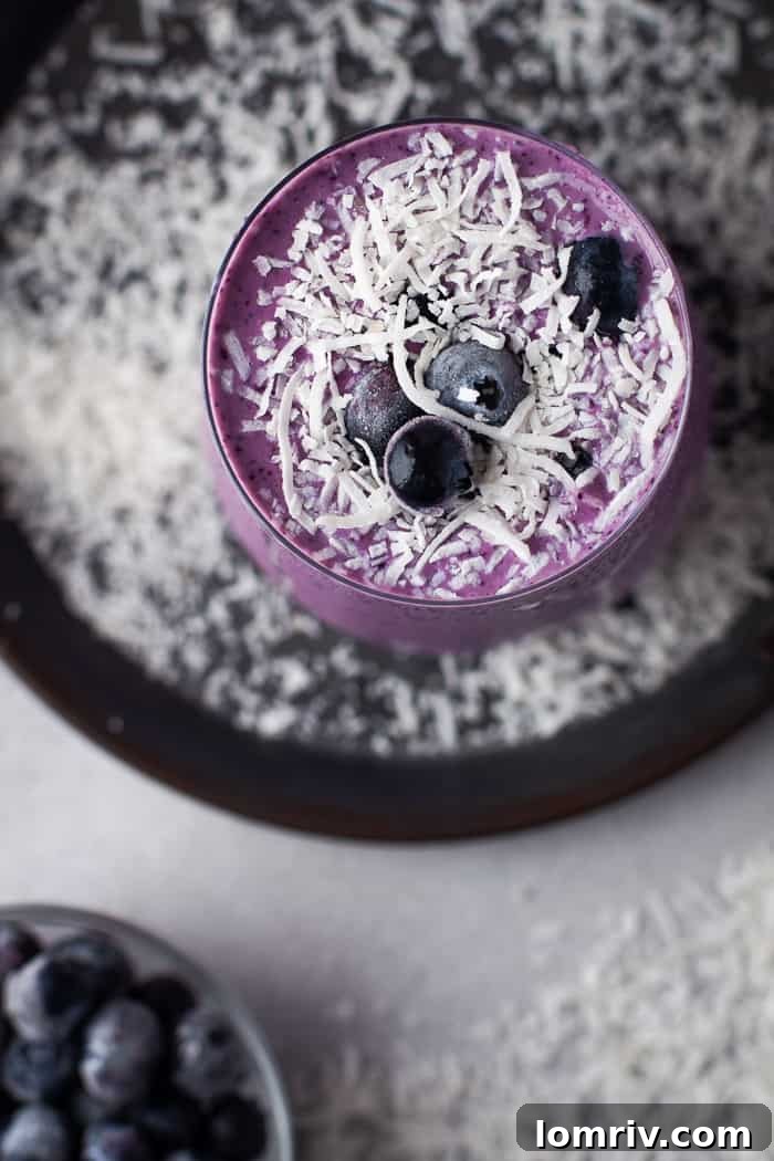Healthy Blueberry Coconut Smoothie in a glass, with unsweetened shredded coconut flakes around it.
