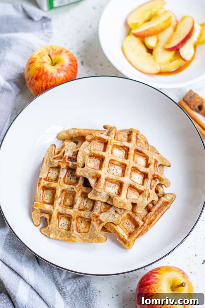 Stacked Apple Cinnamon Waffles drizzled with syrup and fresh apple slices