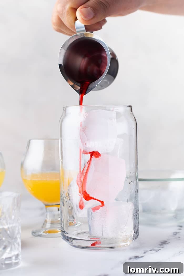 Grenadine being poured into the bottom of an ice-filled glass