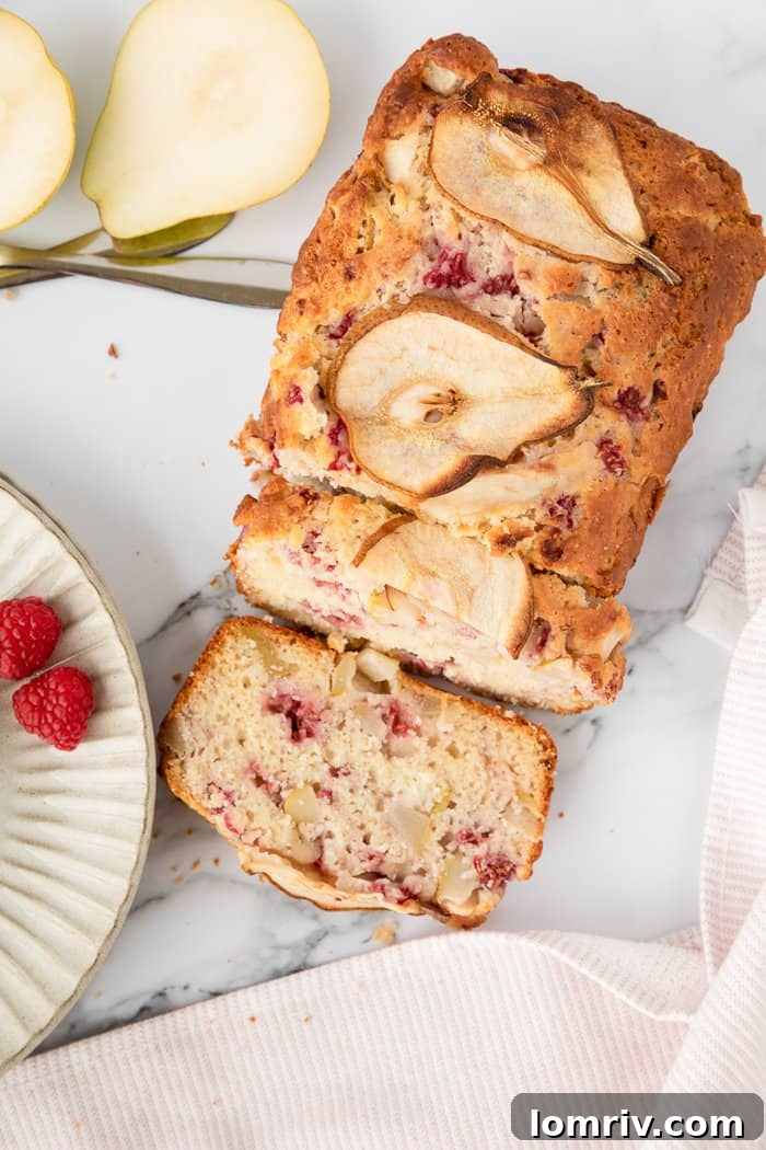 A close-up shot of a thick slice of Pear and Raspberry Bread, revealing its moist texture and fruit pieces, on a marble surface.
