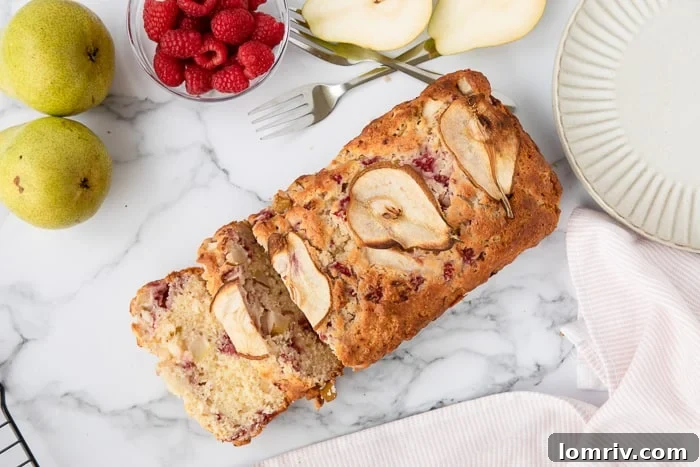 Perfectly sliced Pear and Raspberry Bread arranged on a marble background, surrounded by fresh pears and raspberries.