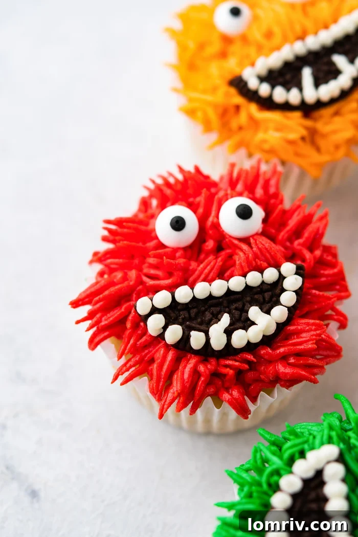 A charming assortment of colorful monster cupcakes with various eyes and Oreo mouths, displayed on a wooden surface.