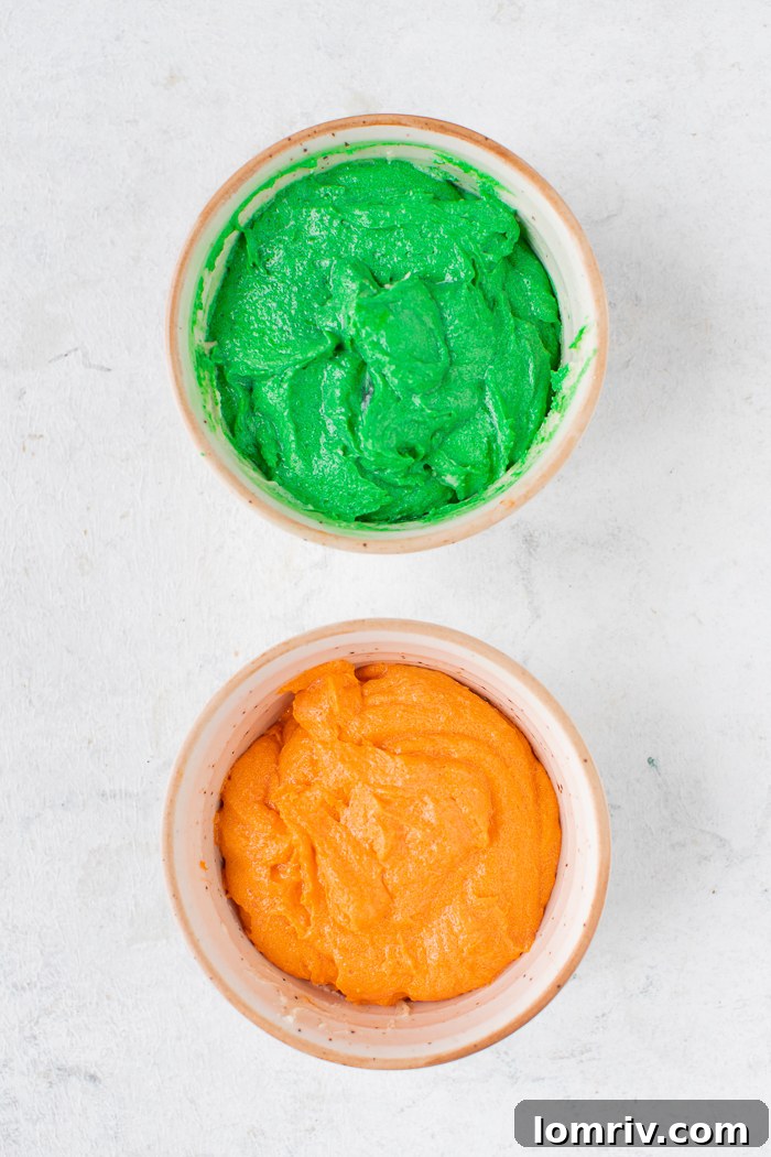 Three bowls of colored frosting (green, orange, red) and one bowl of white frosting, ready for piping.