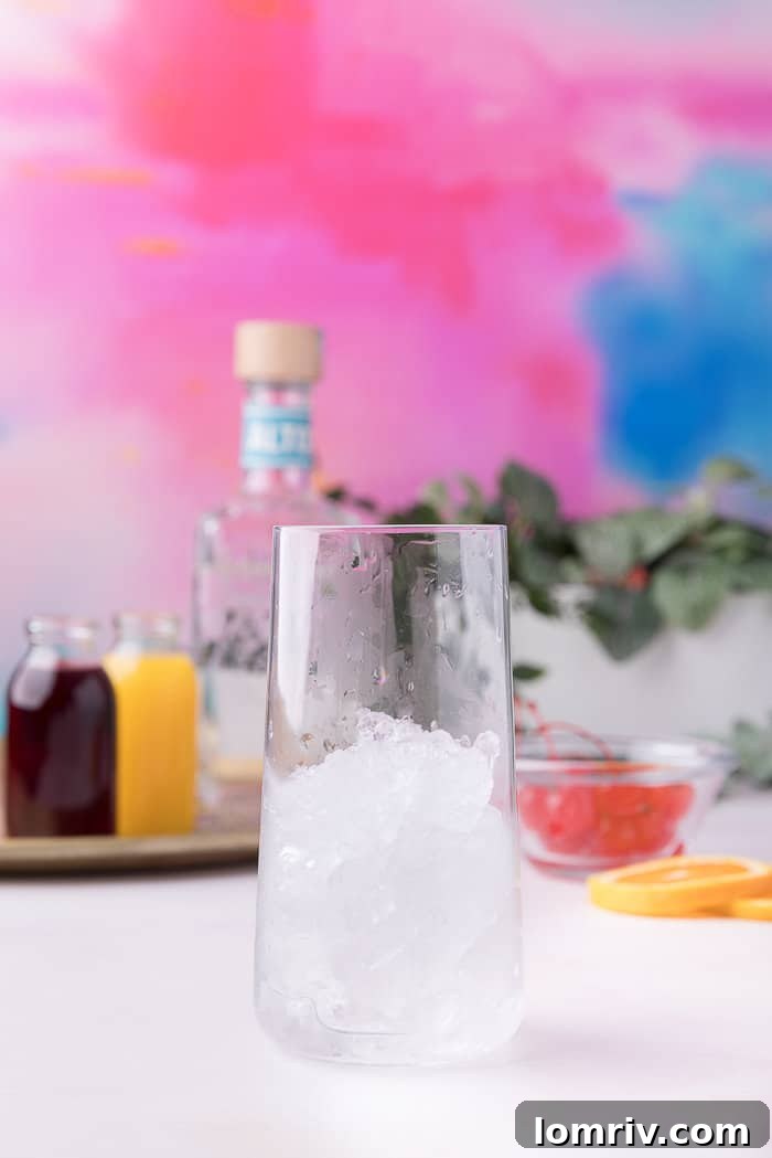 A tall glass being filled with ice, the first step in making a Tequila Sunrise.
