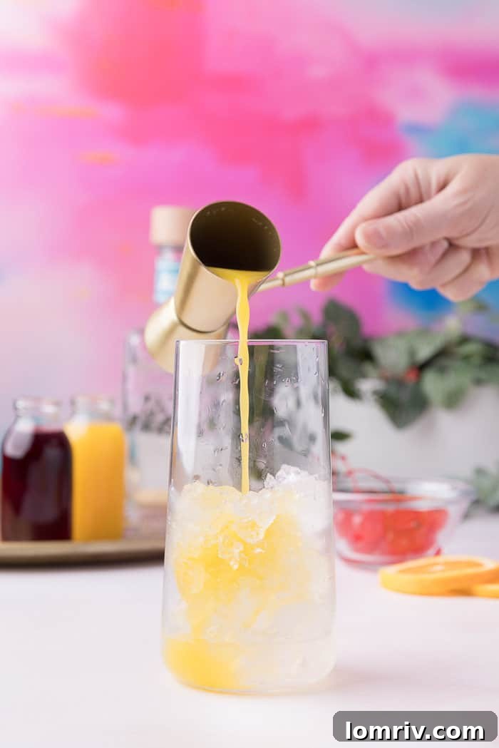 Pouring orange juice into a glass already filled with ice.