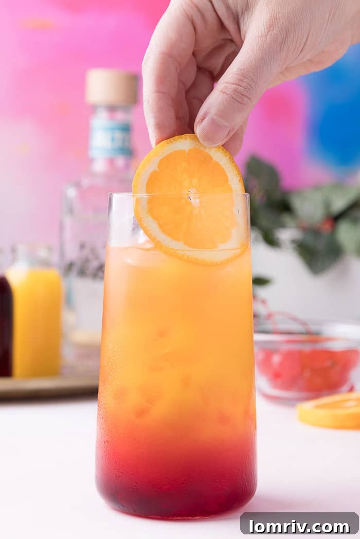 An orange slice and a maraschino cherry being added as garnish to the finished Tequila Sunrise.