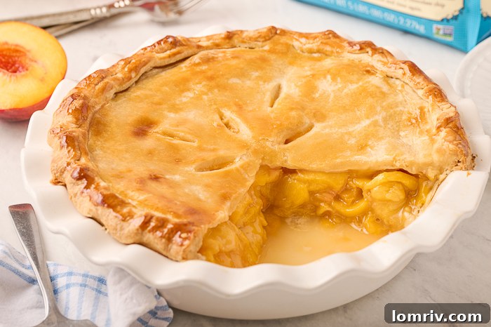 A baked Fresh Peach Pie with decorative crust cooling on a wooden board