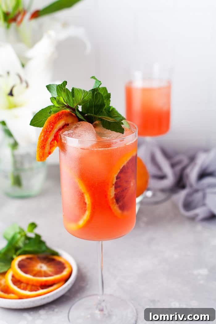 Blood orange cocktail in a glass with blood orange slices, garnishes.