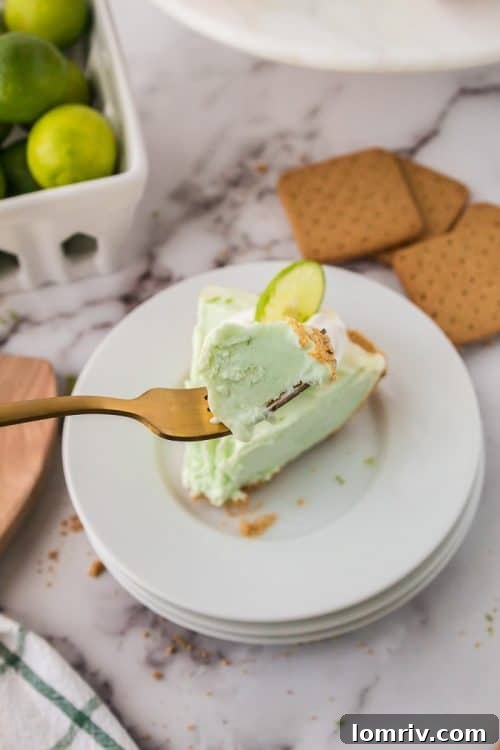 A slice of No Bake Key Lime Pie on a plate with a bite taken out, showing the creamy filling and crust.