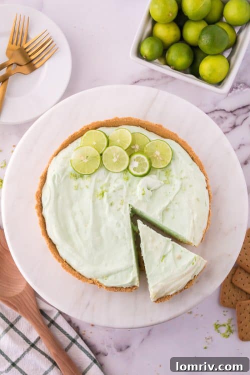 A whole No Bake Key Lime Pie with a slice already cut, revealing the creamy green filling and a perfect graham cracker crust.