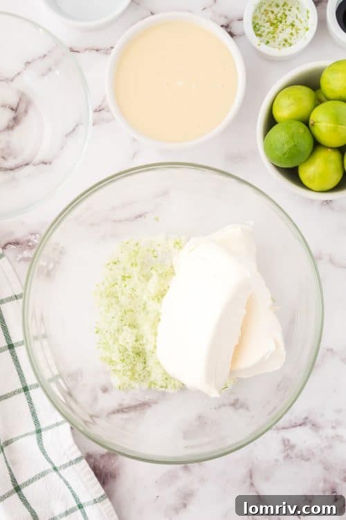 Cream cheese being whipped in a large mixing bowl with an electric mixer, illustrating a key step in preparing the No Bake Key Lime Pie filling.