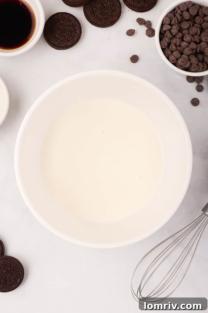 Cold heavy cream and vanilla extract being whipped until stiff peaks form, essential for the light texture of the cheesecake.
