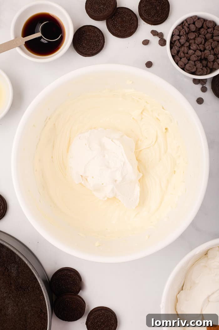 Gently folding the first half of whipped cream into the cream cheese mixture, ensuring a light and airy cheesecake filling.