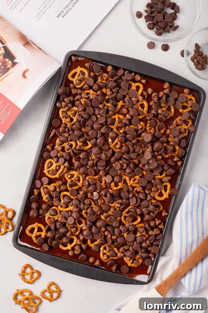 Chocolate chips evenly sprinkled over the pretzel-toffee base, beginning to melt from the residual heat.