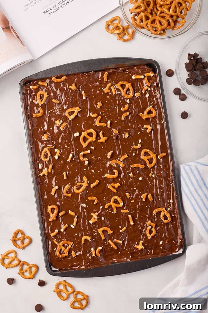 A hand gently pressing crushed pretzels into the melted chocolate layer on the pumpkin bark, adding a finishing touch.
