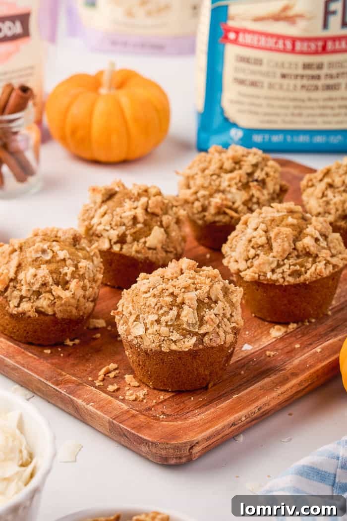 Close-up of three freshly baked pumpkin muffins on a wooden cutting board.