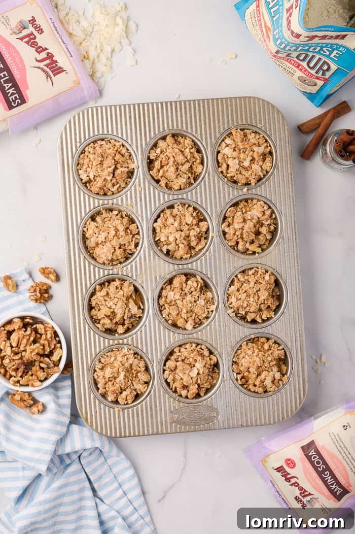 Unbaked pumpkin muffins in a muffin pan, topped with streusel, ready for the oven.