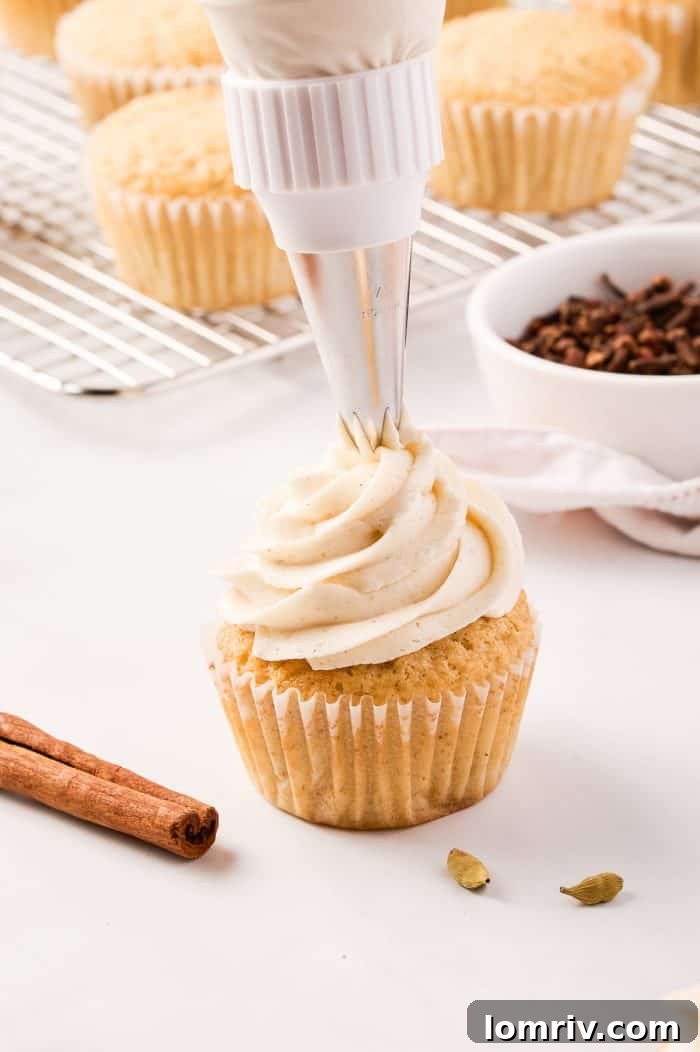 A chai cupcake being expertly frosted with a piping bag, creating an elegant swirl of buttercream.