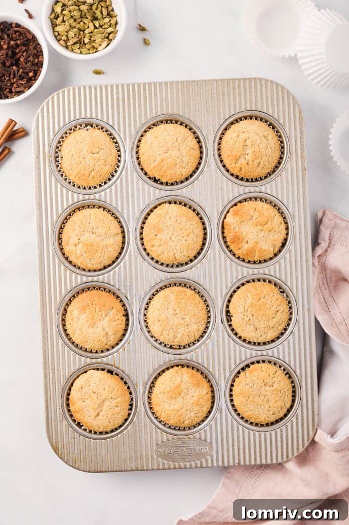A tray of freshly baked chai cupcakes, golden brown and puffed up, straight from the oven.