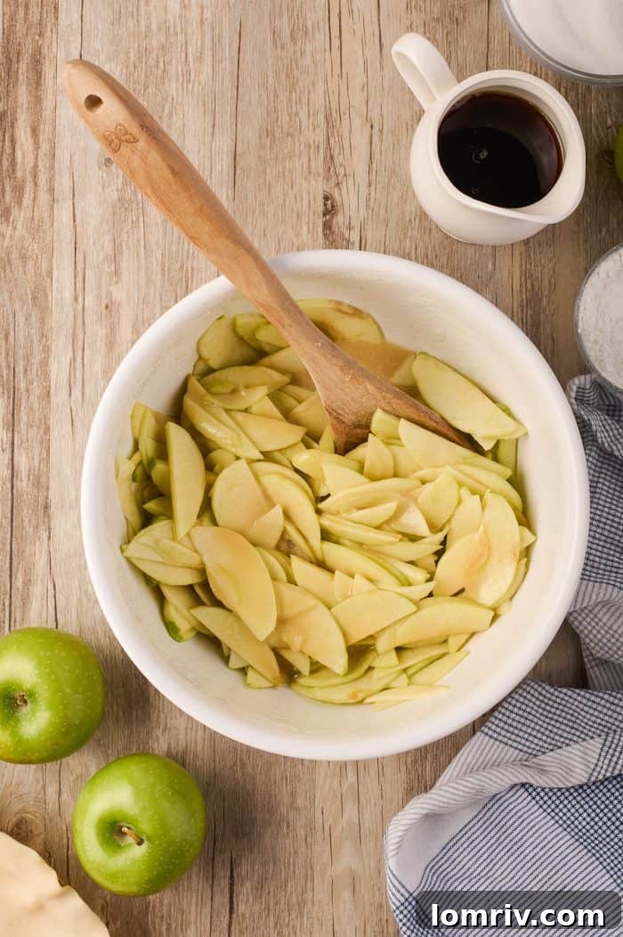 Maple cream apple pie filling, featuring mixed apples, syrup, and cream, in a large bowl.
