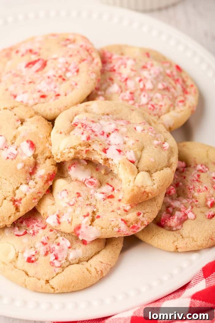 A peppermint white chocolate cookie with a bite taken out of it, revealing its soft interior, white chocolate chips, and crushed candy cane bits.