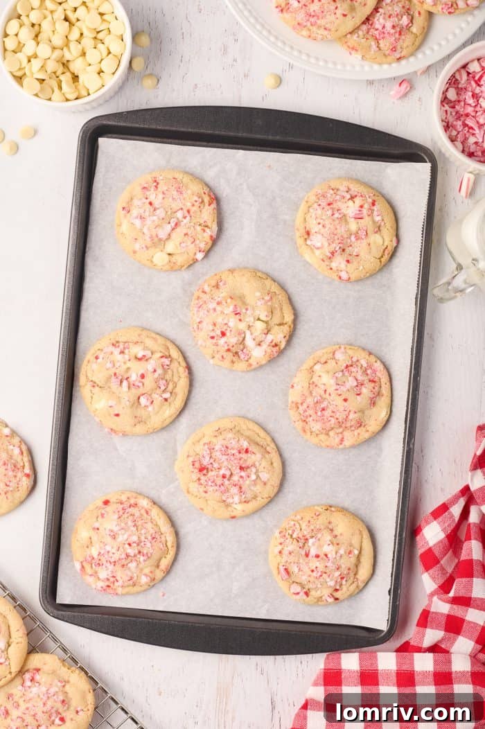 Freshly baked peppermint white chocolate cookies cooling on a wire rack, with some still on the parchment-lined baking tray in the background.